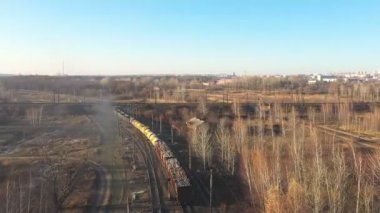 Demiryolu boyunca giden ve endüstriyel malları taşıyan trenin havadan görünüşü. Taşıma vagonları kırsal alandan geçen lokomotifleri takip eden insansız hava aracı. Kargo taşımacılığı ya da teslimat konsepti. Üst görünüm.