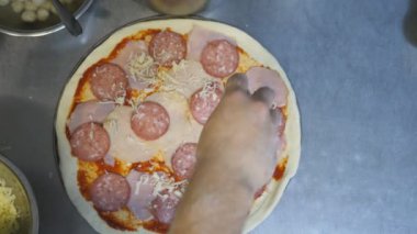 Aşçının eli rendelenmiş peyniri hamur işine koyuyor ve malzemeler mutfakta metal formda. Şef, mutfaktaki ahşap bir yüzey üzerinde pepperoni pizza yapıyor. Yemek hazırlama kavramı. POV Üst Görünümü.