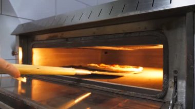 Aşçının erkek eli, pizzayı fırına kürekle koyar ve mutfak restoranında kapatır. Genç aşçı mutfakta fırında lezzetli yemekler pişirecek. Pizzacıda yemek yapma süreci.