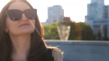 Portrait of beautiful lady in sunglasses walking at sunny day. Attractive brunette girl looks into camera going along city street. Businesswoman commuting to work. Concept of urban lifestyle. Close up