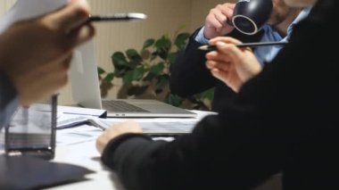 İş gününün sonunda grafikleri inceleyen erkek ve kadın işçilerin elleri. İş ekibi masada oturuyor ve belgeleri kontrol ediyor. Masadaki mali raporları analiz eden iş adamları.