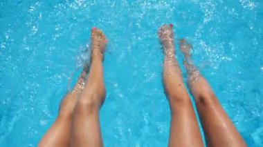 Kadın bacaklarının manzarası otel havuzunda berrak su sıçratıyor. Havzanın kenarında oturan iki arkadaş güneşli bir günde tatilin tadını çıkarıyorlar. Yaz tatili ya da tatil kavramı. Yavaş çekim.