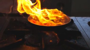 Detail view on flaming skillet in hand of professional chef. Male cook mixing and frying vegetables cooking tasty flambe style dish for visitors of restaurant. Concept of cooking. Slow mo Front view.