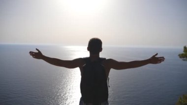Dağın kenarında duran ve muzaffer bir şekilde el kaldıran sırt çantasıyla tanınmayan yürüyüşçü. Erkek turist aktif deniz özgürlüğü ve güzel görünümü zevk gezi sırasında dinleniyor. Yavaş mo Geri görünüm.