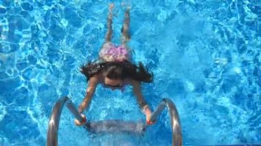 Attractive woman in pink bikini getting out of pool. Young sexy girl enjoying summer vacation refreshing in basin. Lady in sunglasses relaxing on resort. Travel or holiday concept. Slow mo Top view.