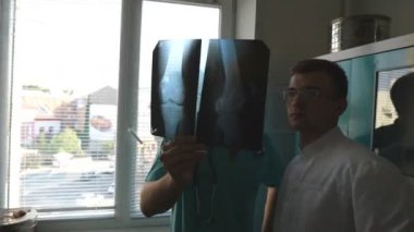 Hastanedeki tıp çalışanları röntgen izlerini inceliyor. Kafkasyalı iki doktor MRI resmine bakıp bunu tartışıyor. Erkek doktorlar röntgen görüntülerine bakarken birbirlerine danışıyorlar. Kapat..