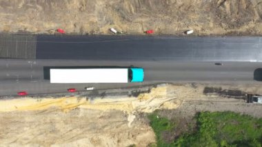 Yol çalışması sırasında yeni otobanda beyaz römorklu bir kamyonun hava görüntüsü. Kamyon üzerinde uçan İHA taşıma kargo taşıma kırsal karayolu boyunca. Otoyol trafiği. Taşıma konsepti. Üst görünüm.