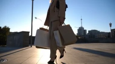 Genç kız şehir caddesinde yürüyen kağıt paketler taşıyor. Güzel bir kadın alışveriş sonrası alışveriş çantalarını şehir meydanında tutuyor. Satış ve indirim kavramı. Düşük görünüm Yavaş çekim Yakın çekim.