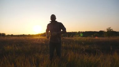 Close up of happy man running through grass field with sunset at background. Young guy jogging among summer meadow. Male enjoying rest at beautiful nature. Concept of carefree and freedom. Slow mo.