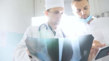 Hastanın röntgen görüntüsü hakkında birbirlerine danışırlarken tablet kullanan sağlık görevlileri. Hastanedeki tıp çalışanları röntgen izlerini inceliyor. Kafkasyalı iki doktor MRI fotoğrafına bakıp bunu tartışıyor.