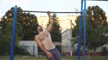 Spor sahasında tek elle barfiks çeken bir sporcu. Genç sporcu açık havada yatay bar eğitimi alıyor. Kas sporcusu egzersiz sırasında güç egzersizleri yapıyor. Sağlıklı yaşam tarzı kavramı.