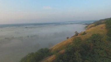 Sabahın erken saatlerinde güzel doğa manzarasının hava görüntüsü. Dağın zirvesi ve vadisinin yoğun sisle kaplı muhteşem manzarası. Harika bir kırsal alanın üzerinde uçmak. Yavaş çekim.
