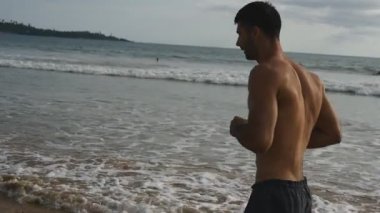 Genç sporcu adam okyanus kıyısında koşuyor. Atletik yakışıklı adam güzel bir deniz manzarası arka planında koşuyor. Erkek sporcu deniz kıyısında egzersiz yapıyor. Sağlıklı aktif yaşam tarzı kavramı. Yavaşça kapat..