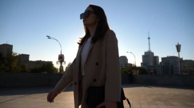 Kendine güvenen bir iş kadını işe gidip geliyor. Güneş gözlüklü güzel bayan yüksek topuklu ayakkabılarla kaldırımda yürüyor. Çekici esmer kız arka planda güneş ışığıyla şehir caddesinde dolaşıyor. Yavaş çekim.