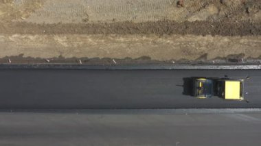 Buharlı silindirin yeni asfalt tabakasını sererken havadan çekilmiş görüntüsü. Kırsal bölgedeki yol yapım sürecinin üst görüntüsü. Ağır makineler üzerinde uçan İHA otoyolu onarıyor. Endüstri kavramı.