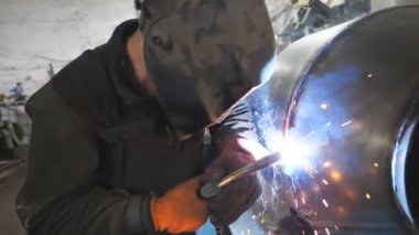 Kaynakçı iki çelik detay arasında ortaklık yapıyor. Adam metal parçalarını birbirine kaynaştırıyor. Metal fabrikasında koruyucu maske kaynak işçisi. Yavaş çekim. Yakın çekim..