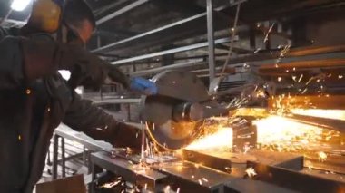 Atölyede çeliği kesen dairesel testereli sanayi işçisi. Güvenlik koruması altındaki adam metal kesmek için testere kullanıyor. Zanaatkar metali öğütüyor. Sıcak metalden kıvılcımlar çıkıyor. Yavaş çekim.