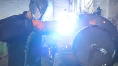 Endüstriyel üretimde koruyucu maske kaynak işçisi. Kaynakçı, metal fabrikasında iki çelik detayı arasında bağlantı kuruyor. Metal kaynak yapan adam. Yavaşça kapat..