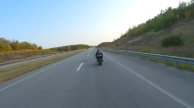 Anayolda motosiklet süren motosikletliyi takip edin. Motosikletli, kır yolunda motosikletiyle yarışıyor. Yolculuk sırasında bisiklet süren adam. Yolculukta özgürlük ve macera kavramı. Hava görüntüsü.