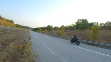 Anayolda motosiklet süren motosikletliyi takip edin. Motosikletli, kır yolunda motosikletiyle yarışıyor. Yolculuk sırasında bisiklet süren adam. Yolculukta özgürlük ve macera kavramı. Hava görüntüsü.