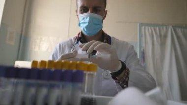 Bilim adamı COVID-19 için tedavi geliştiriyor. Laboratuvarda çalışan bir doktor. Tıbbi maske takan doktor ve eldivenler şırınga kullanarak test tüplerini sıvıyla dolduruyor. Sağlık ve koronavirüs salgını kavramı.