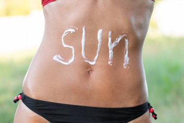 Bronzlaşmış bir kadının karnına güneş kremi sürüyorum. Plajda güneş koruması kullanıyorum..