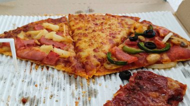 Peynir, jambon, sosis ve dolma biberle süslenmiş dilimlenmiş pizza.