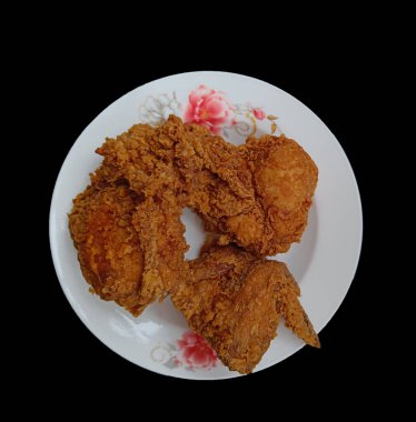 Kızarmış tavuk tabakta, siyah arka planda.