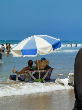 Koca ve karısı yaz tatili boyunca okyanus suyunda sandalyelerinde dinleniyorlar.