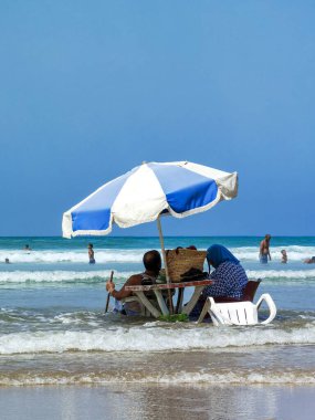 Koca ve karısı yaz tatili boyunca okyanus suyunda sandalyelerinde dinleniyorlar.