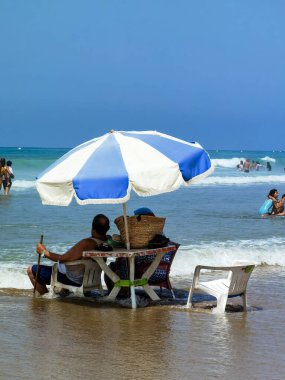 Koca ve karısı yaz tatili boyunca okyanus suyunda sandalyelerinde dinleniyorlar.