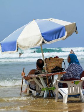 Koca ve karısı yaz tatili boyunca okyanus suyunda sandalyelerinde dinleniyorlar.