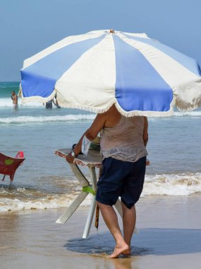 Masasını şemsiyeyle tutan ve kıyıya doğru yürüyen tanınmamış bir adam.