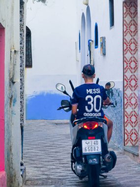 Genç Faslı bir adam motosikletiyle Asilah 'ta bir caddeden geçiyor.