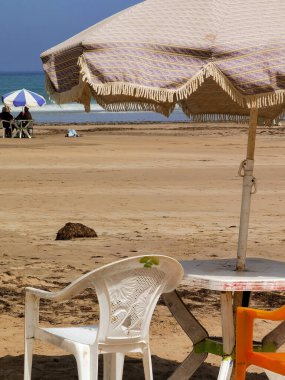 Fas sahilinde sandalyeli ve şemsiyeli bir masa, Asilah.