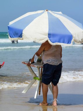 Masasını şemsiyeyle tutan ve kıyıya doğru yürüyen tanınmamış bir adam.