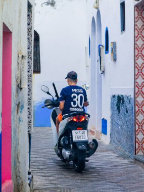 Genç Faslı bir adam motosikletiyle Asilah 'ta bir caddeden geçiyor.