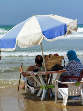 Koca ve karısı yaz tatili boyunca okyanus suyunda sandalyelerinde dinleniyorlar.