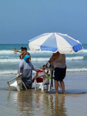 Koca ve karısı yaz tatili boyunca okyanus suyunda sandalyelerinde dinleniyorlar.