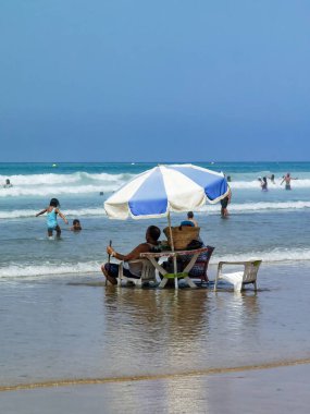 Koca ve karısı yaz tatili boyunca okyanus suyunda sandalyelerinde dinleniyorlar.