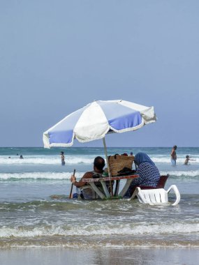 Koca ve karısı yaz tatili boyunca okyanus suyunda sandalyelerinde dinleniyorlar.