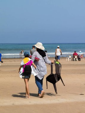 Fas sahilinde genç bir çocukla yürüyen bir kadın.