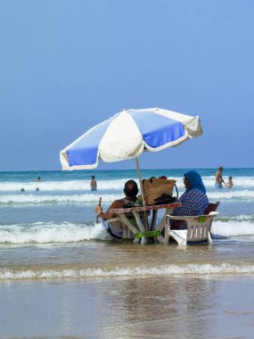 Koca ve karısı yaz tatili boyunca okyanus suyunda sandalyelerinde dinleniyorlar.