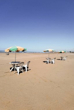 Fas sahilinde beyaz sandalyeli ve şemsiyeli birkaç masa.