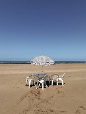 Fas sahilinde beyaz sandalyeli ve şemsiyeli bir masa.