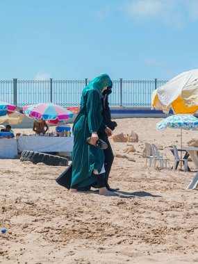 Müslüman kadınlar sahilde birlikte yürüyorlar.