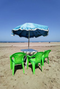 Fas sahilinde yeşil sandalyeli ve mavi şemsiyeli bir masa.