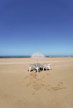 Fas sahilinde beyaz sandalyeli ve şemsiyeli bir masa.