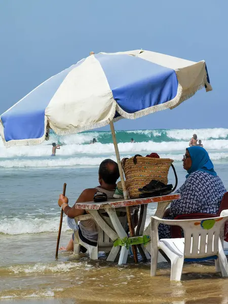 Koca ve karısı yaz tatili boyunca okyanus suyunda sandalyelerinde dinleniyorlar.