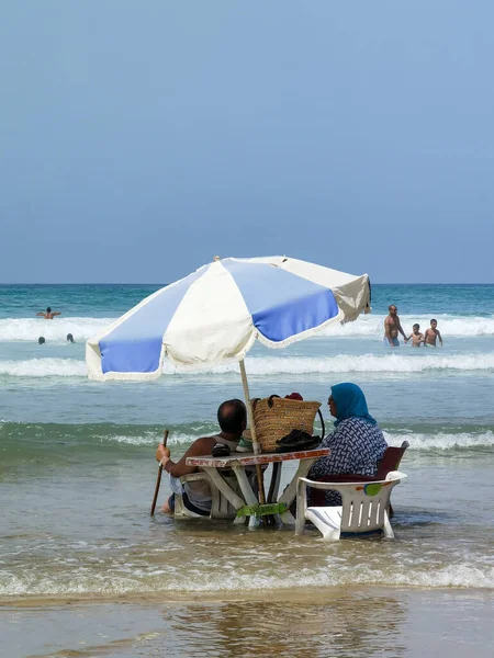 Koca ve karısı yaz tatili boyunca okyanus suyunda sandalyelerinde dinleniyorlar.